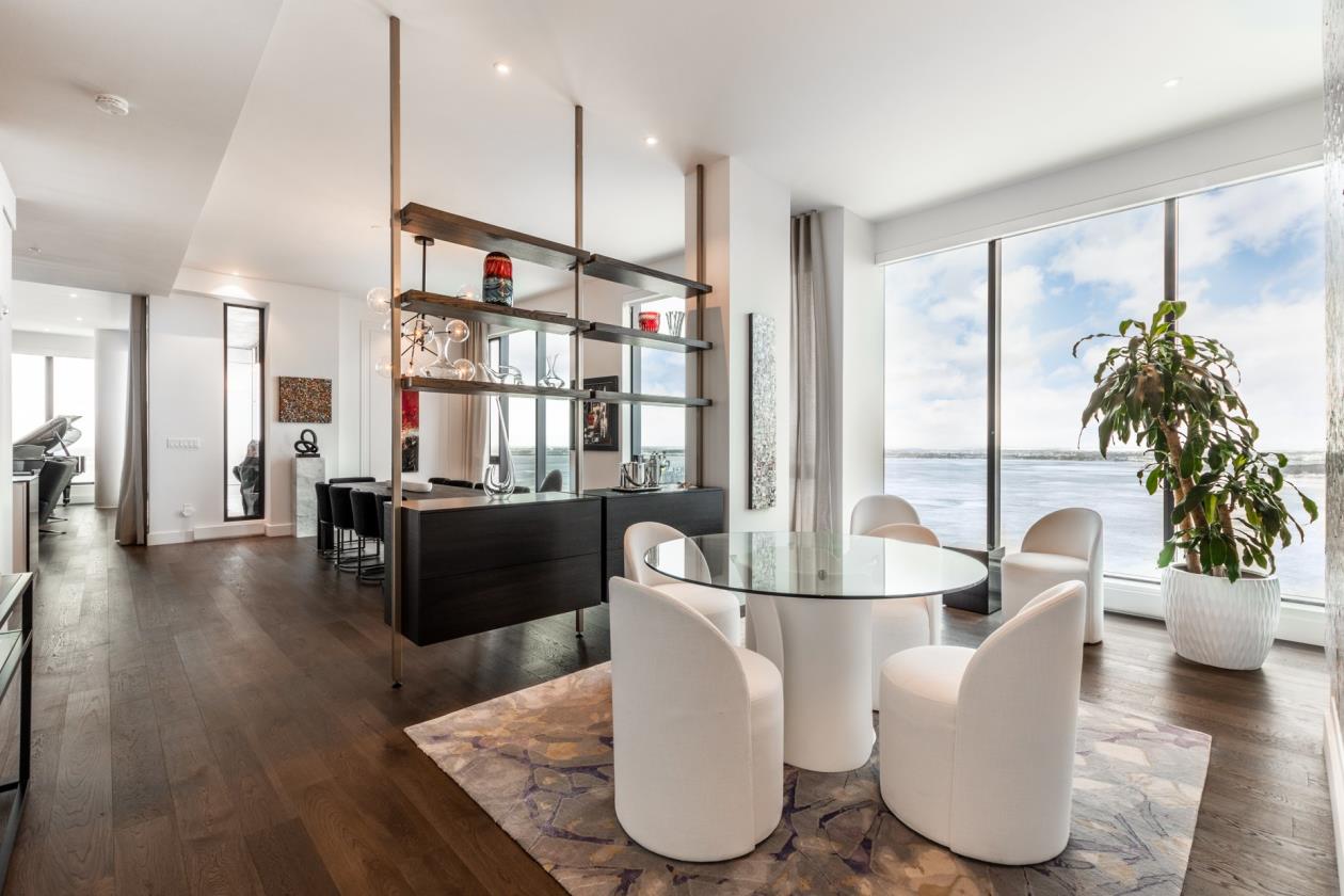 Table ronde en verre avec fauteuils en tissus blanc donnant sur une vaste fenestration avec vue sur le fleuve